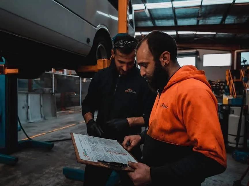 Two Skylight Buslines mechanics working through a maintenance checklist beneath a raised coach